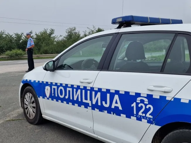 Policijsko vozilo sa natpisom "POLICIJA 122" i policijski službenik u uniformi na putu.