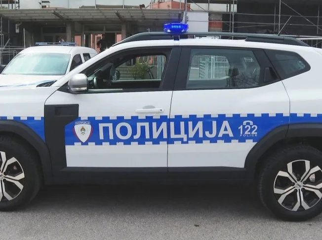 Bijelo policijsko vozilo sa plavom rotacijom na krovu i natpisom "POLICIJA" i "122 POLICE" na boku.