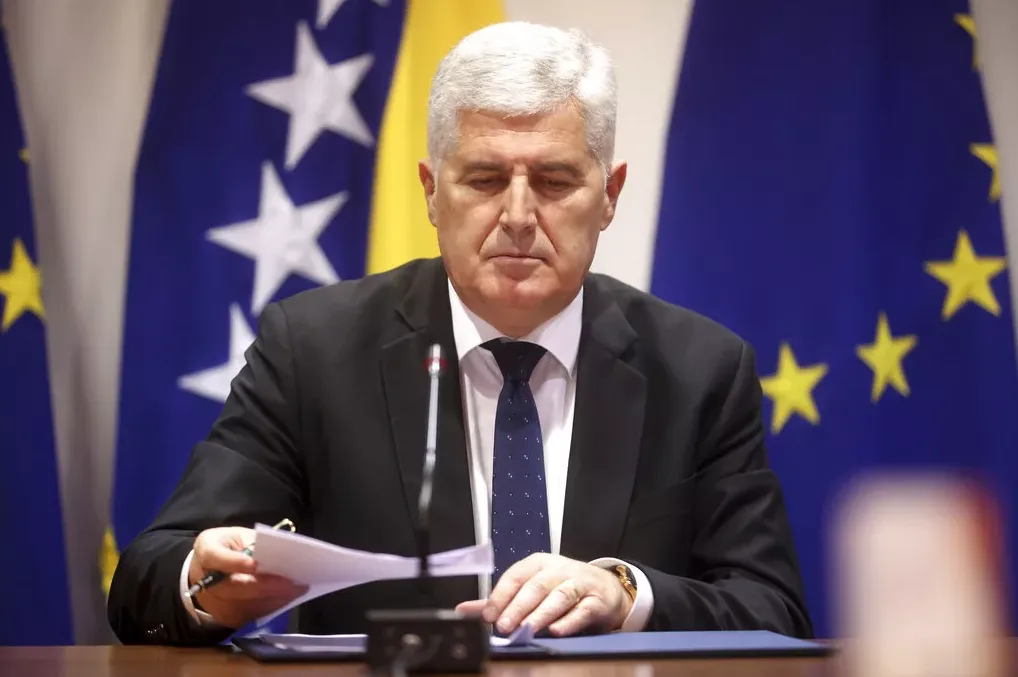 Dragan Čović sjedi za stolom s papirima, ispred zastava Bosne i Hercegovine i Evropske unije.