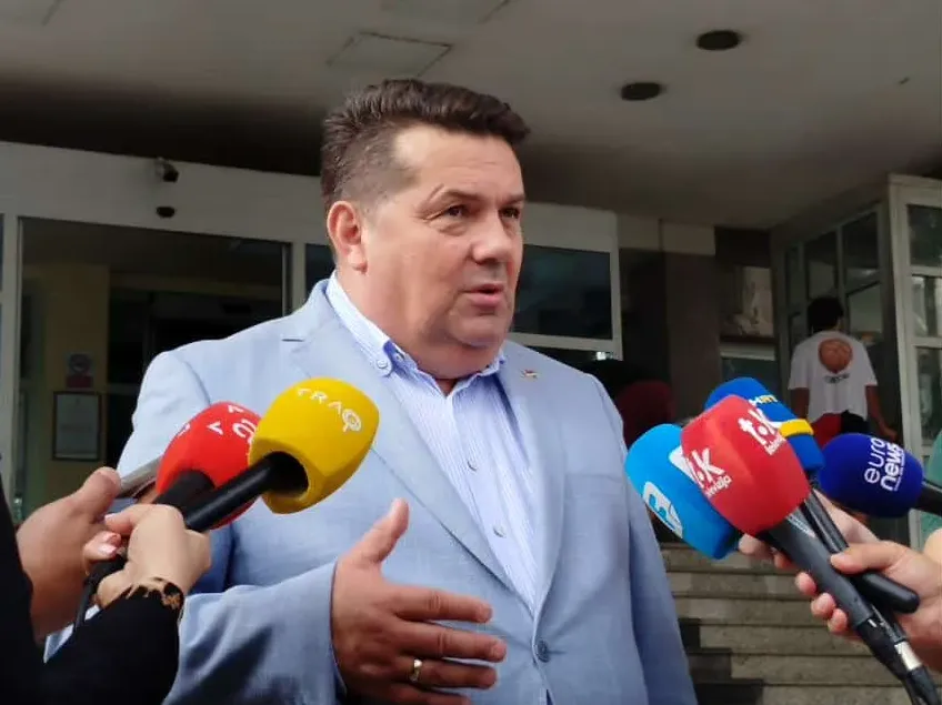 Političar u svijetlo plavom odijelu daje izjavu za više medija, sa mikrofonima ispred sebe.