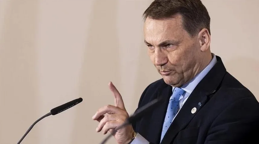 Političar u tamnom odijelu i plavoj kravati sa tačkicama drži govor iza mikrofona.