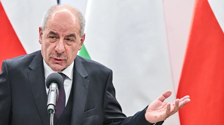 Muškarac u crnom odijelu govori iza mikrofona, sa podignutom rukom u gestu.