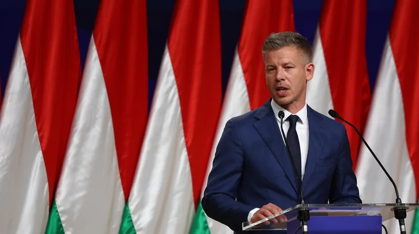 Političar u tamnom odijelu govori iza govorničkog postolja s dva mikrofona, a u pozadini se vide zastave Mađarske.