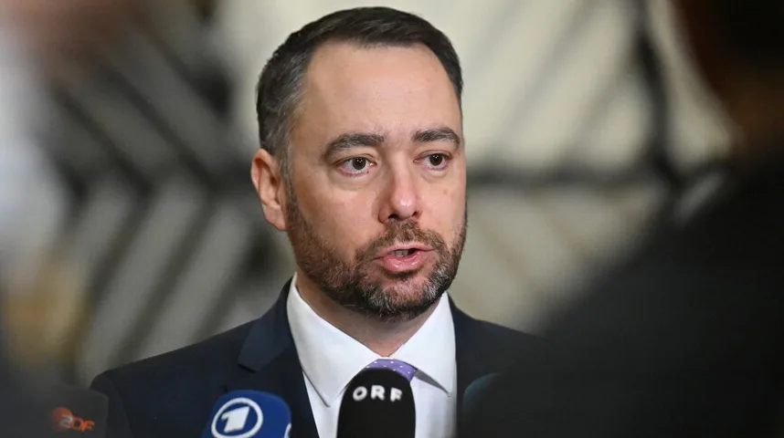 Političar sa bradom i bijelom košuljom i ljubičastom kravatom govori u mikrofon ispred novinara.