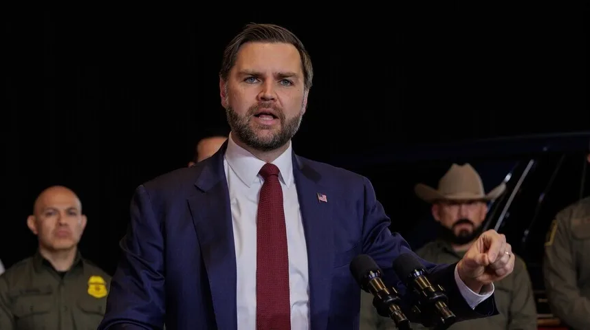 Političar sa gustim smeđim bradom i tamnim odijelom govori na tribini.