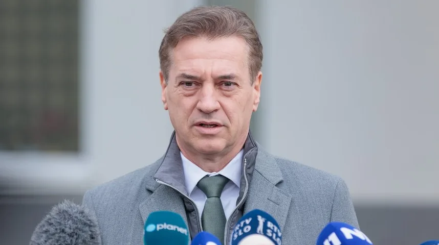 Političar u sivom kaputu sa zelenom kravatom ispred mikrofona medija