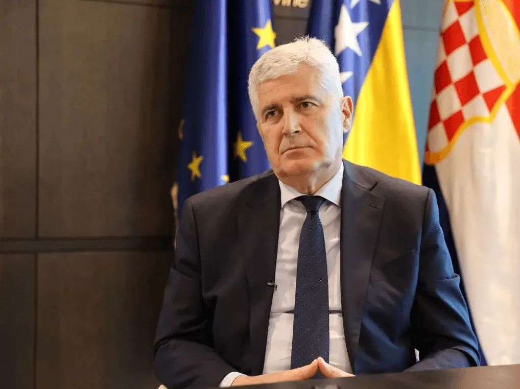 Dragan Čović, predsjednik HDZ-a BiH, sjedi u odijelu i kravati, sa zastavama Bosne i Hercegovine i Evropske unije iza njega.