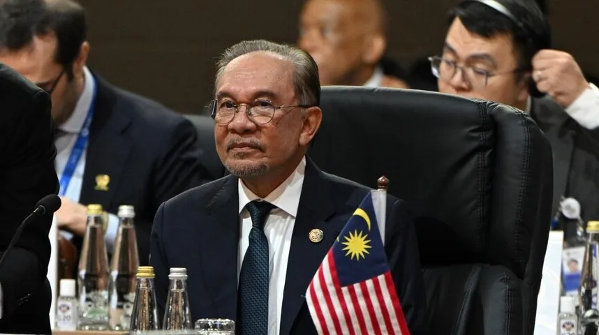 Muškarac u odijelu sa naočalama i malom zastavom Malezije ispred sebe