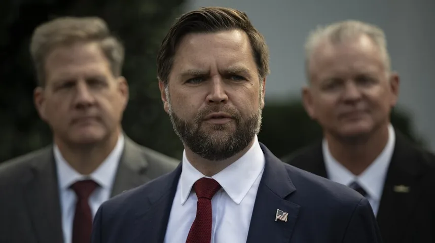 Političar s bradom u tamnom odijelu i crvenoj kravati sa američkom zastavicom na reveru.