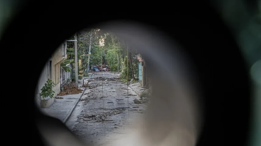 Prizor oštećene ulice sa ruševinama i smećem nakon oluje, gledano kroz okrugli otvor.