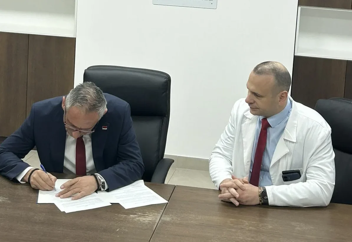 Dva muškarca za stolom, jedan potpisuje dokumente, drugi nosi bijeli mantil.