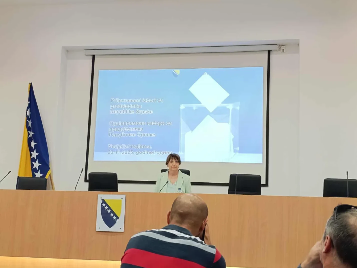 Gospođa sjedi za govornicom ispred projektora na kojem piše "Prijevremeni izbori za predsjednika Republike Srpske" i datum "23.11.2025."