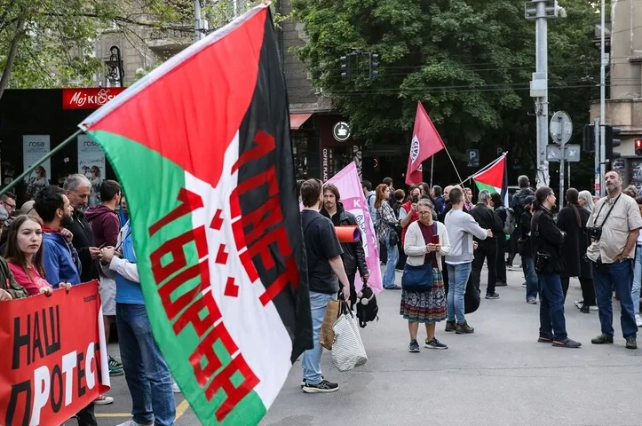 Grupa ljudi na protestu, neki nose palestinske zastave i transparente sa natpisom „Naš protest“