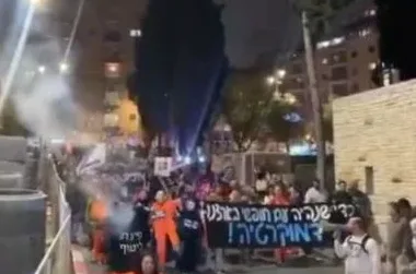 Grupa ljudi drži transparent na kojem piše na hebrejskom tokom protesta noću.