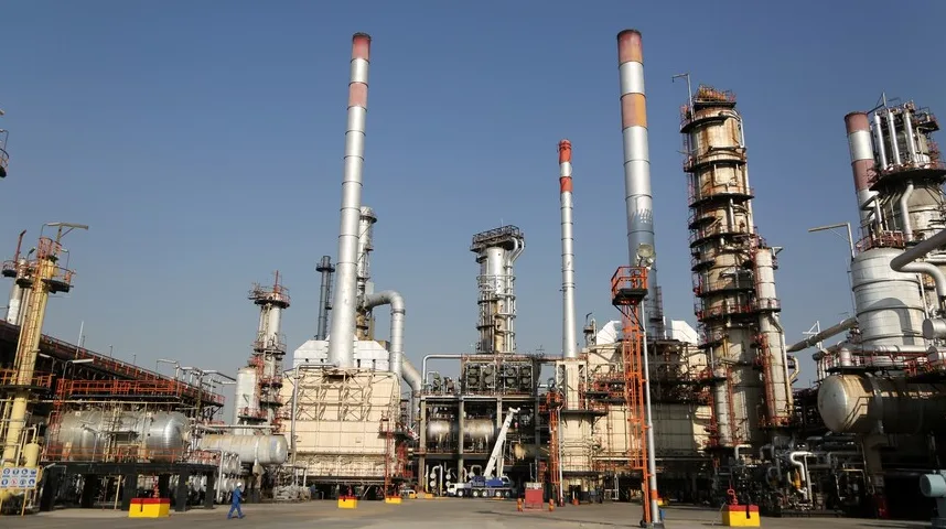 Industrijsko postrojenje rafinerije nafte sa visokim dimnjacima i kompleksnom mrežom culjevaca i instalacija, pod vedrim plavim nebom.