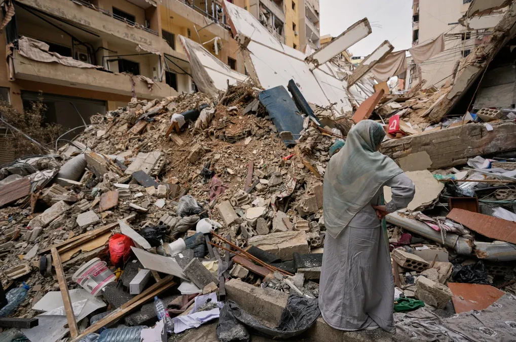 Žena u hidžabu stoji okrenuta leđima, gledajući u ogromnu gomilu ruševina uništene zgrade.