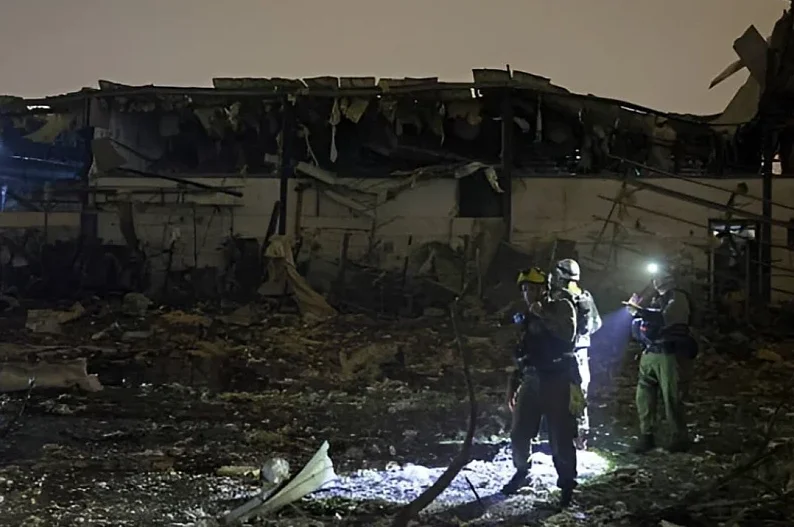 Grupa spasilaca u opremi sa naglavnim lampama vrši uviđaj na zgarištu uništene zgrade noću.
