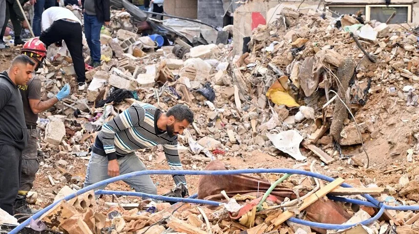 Ljudi u civilnoj odjeći i spasioci pretražuju ruševine porušenog objekta, tražeći preživjele ili materijalne dokaze nakon nesreće.
