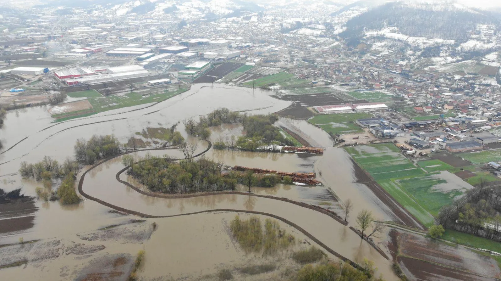 Područje pogođeno poplavom prikazano iz zraka, sa poplavljenim rijekama, poljima i dijelom urbanog naselja s industrijskim objektima.