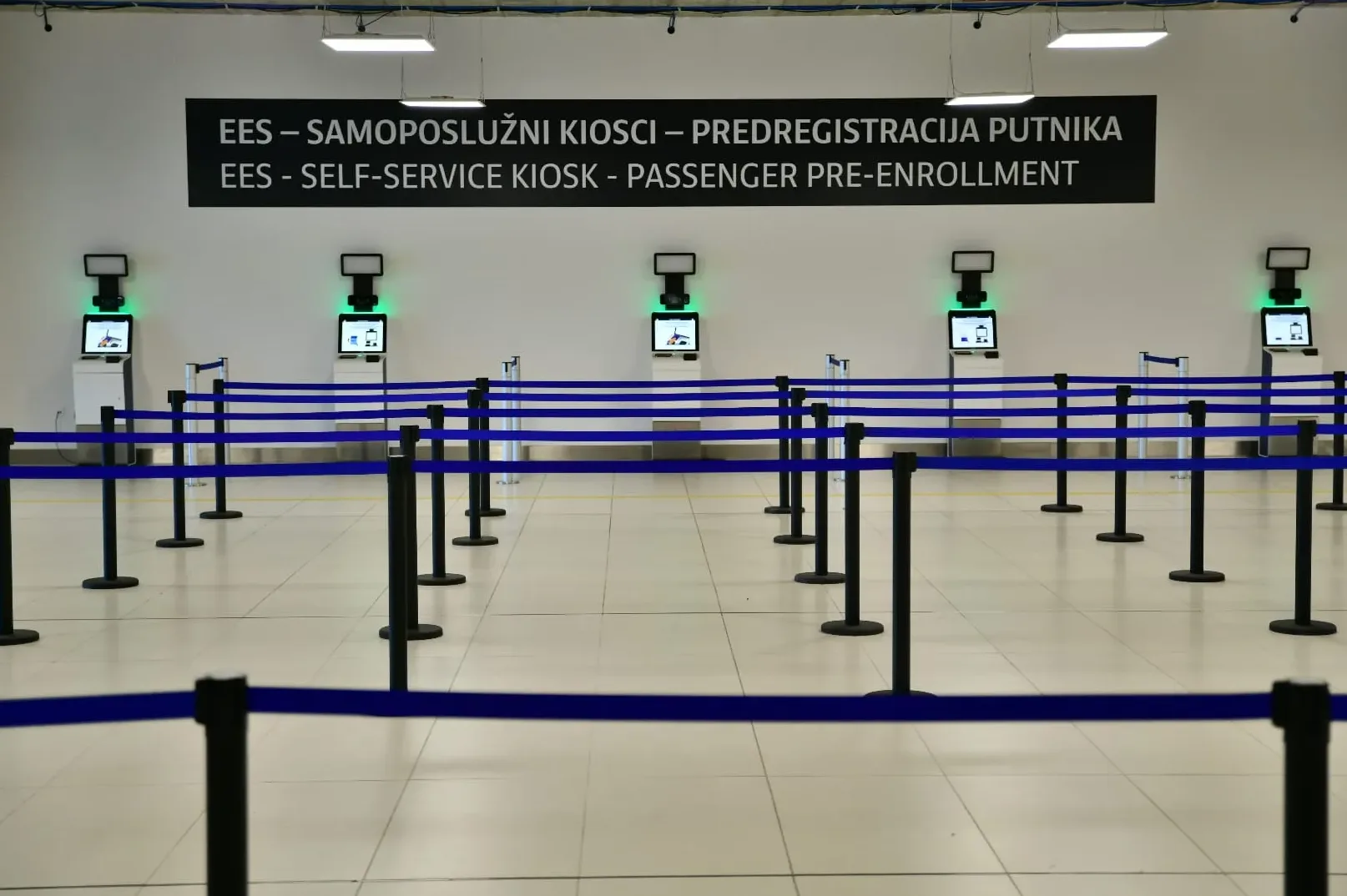 Samoposlužni kiosci za predregistraciju putnika sa plavim trakama za redove.