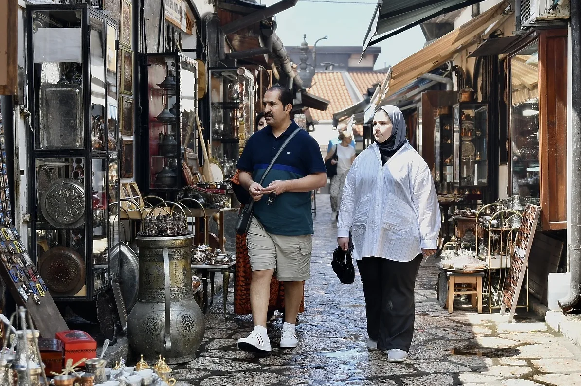 Muškarac i žena hodaju ulicom prepunom tezgi sa suvenirima i starinama na Baščaršiji.