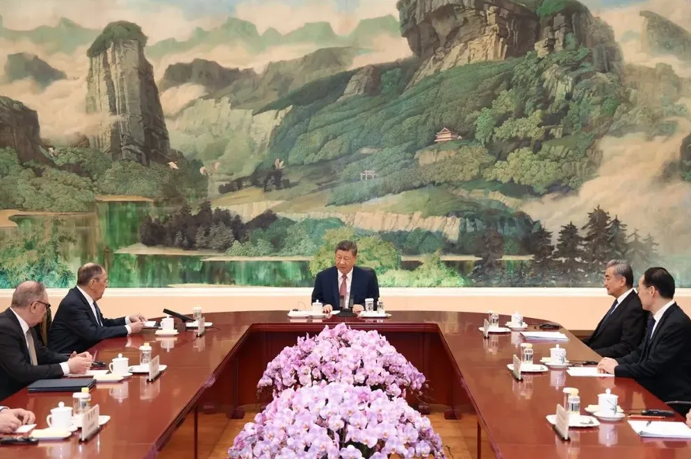 Xi Jinping sjedi za stolom sa sastanka sa zvaničnicima iz Rusije, kao što su Sergej Lavrov i drugi, ispred tradicionalnog kineskog murala sa planinama i rijekama.