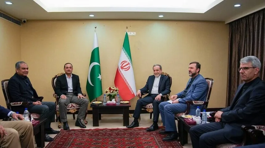 Grupa muškaraca u odijelima sjedi na sastanku, sa zastavama Pakistana i Irana u pozadini.