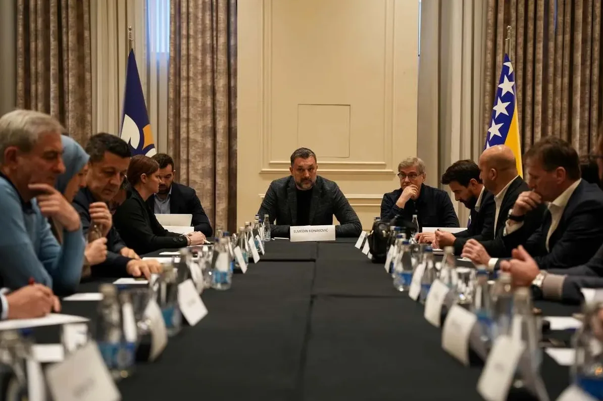 Političari sjede za dugim stolom na sastanku u Bosni i Hercegovini, s zastavom Bosne i Hercegovine u pozadini.