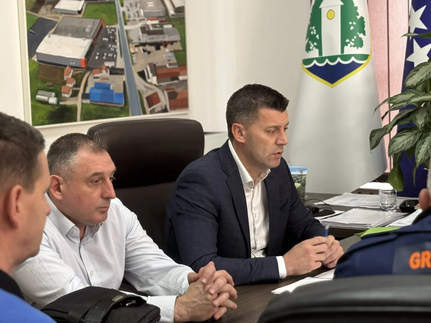 Dva muškarca sjede za stolom u kancelariji, a jedan od njih drži olovku i gleda u dokumenta.