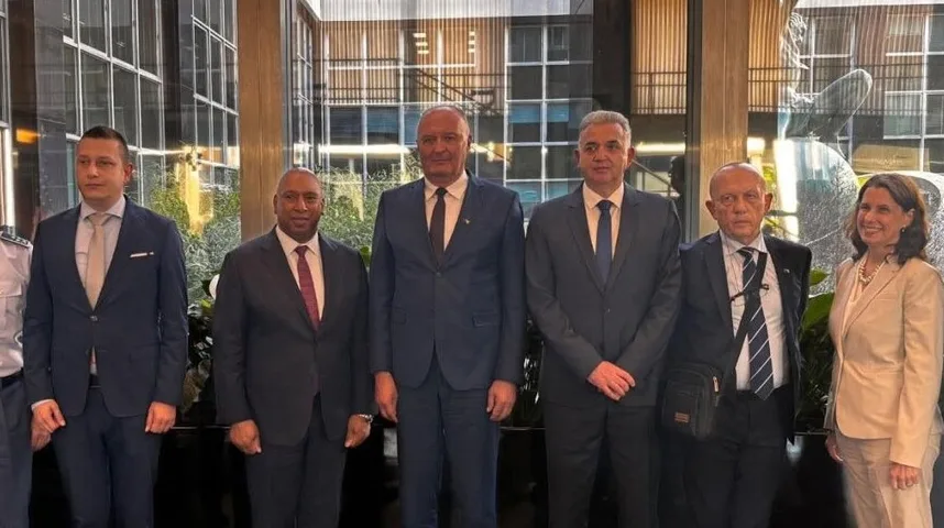 Grupa od šest osoba, pet muškaraca i jedna žena, pozira za fotografiju u unutrašnjosti zgrade sa staklenom fasadom i skulpturom u pozadini.