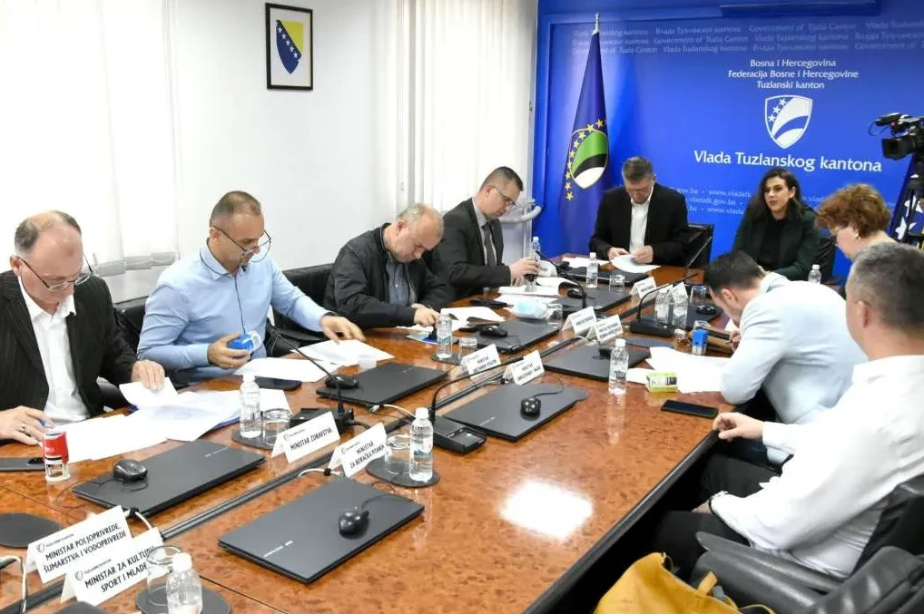 Sastanak zvaničnika Vlade Tuzlanskog kantona za drvenim stolom sa dokumentima i laptopima ispred njih.