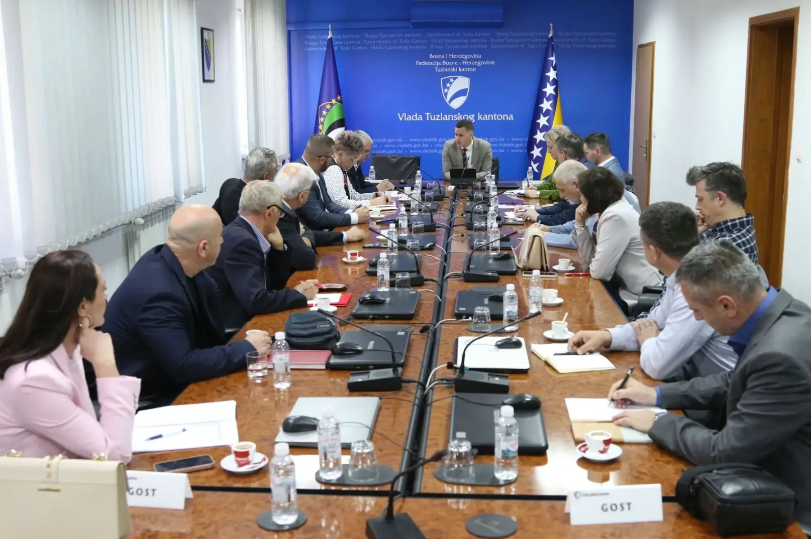 Sjednica Vlade Tuzlanskog kantona sa brojnim učesnicima, fokus na radnom stolu sa laptopima, mikrofonima i dokumentima.