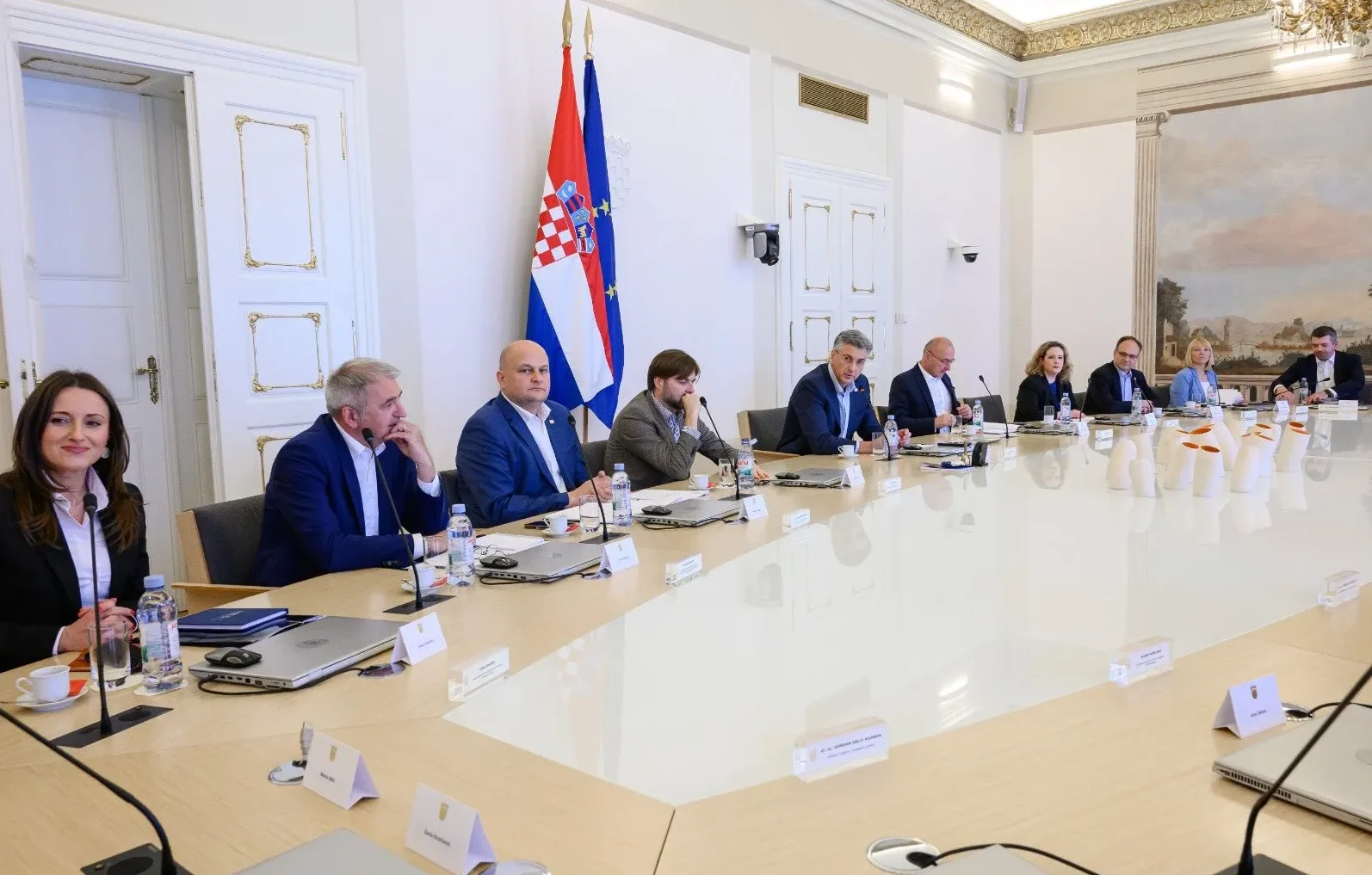 Grupa vladinih duznosnika sjedi za dugim stolom tokom sastanka u elegantnoj prostoriji sa zastavama Hrvatske i Evropske Unije u pozadini.