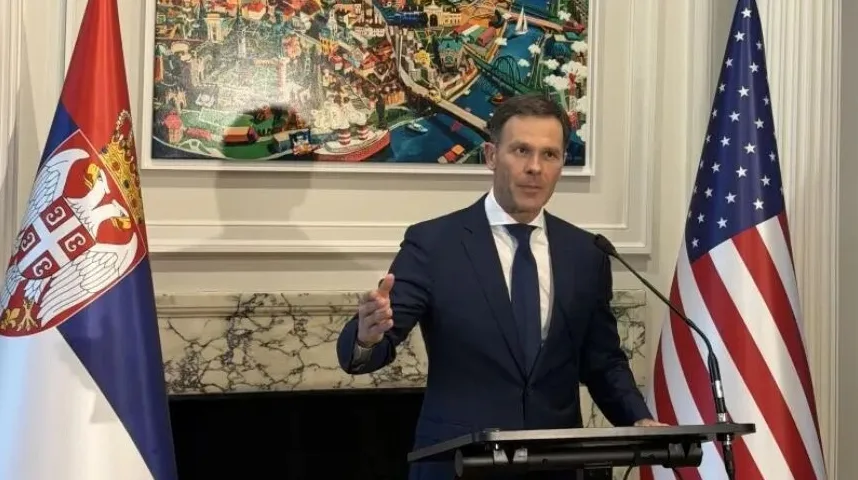 Političar u tamnom odijelu govori pored zastave Srbije i Sjedinjenih Američkih Država.