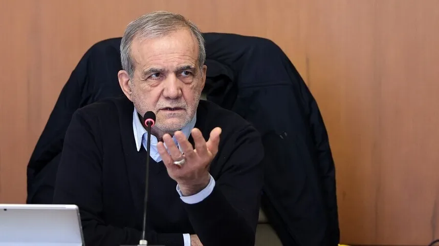 Starji gospodin sa sivom kosom, obučen u crni džemper preko plave košulje, sjedi za stolom i govori podignutih ruku, sa mikrofonom ispred sebe.