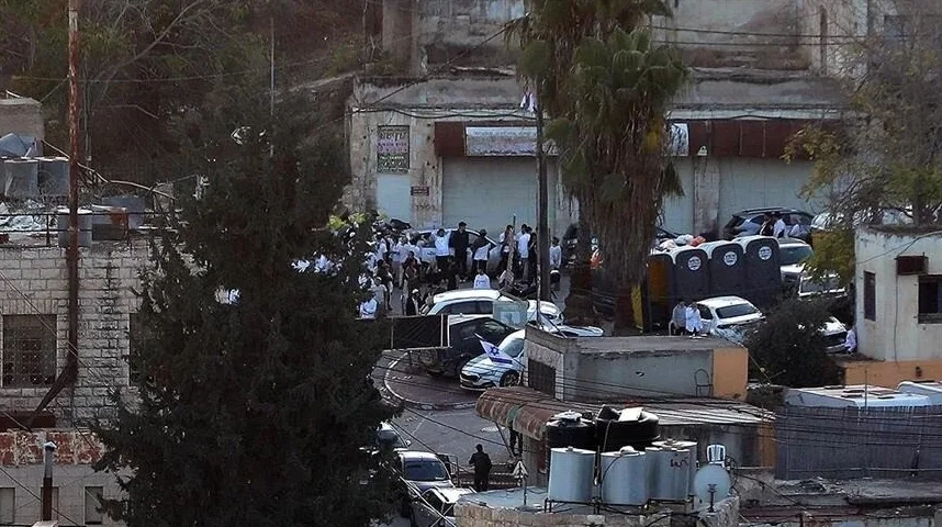 Skupina ljudi okupljena oko vozila na ulici, s nekoliko prenosivih toaleta u pozadini.