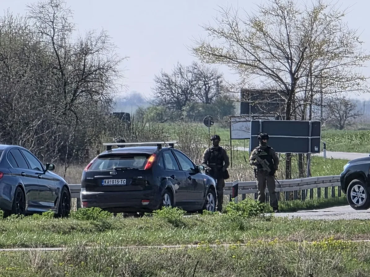 Dva službenika u uniformama, naoružana, stoje pored puta.