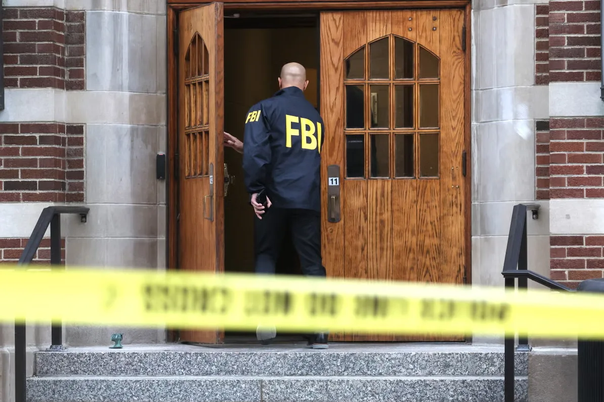 Federalni istražni biro (FBI) agent u crnoj jakni s natpisom "FBI" ulazi kroz drvena vrata zgrade.