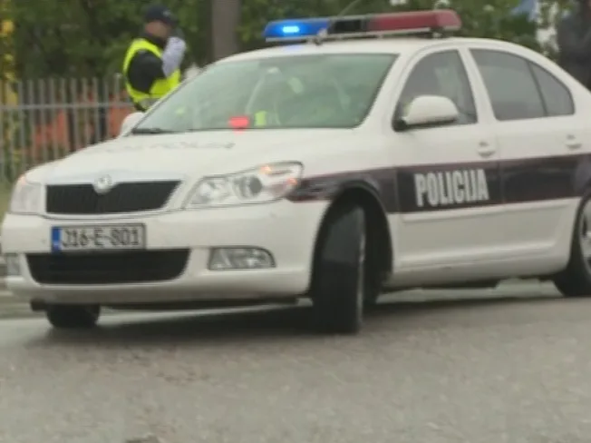 Bijelo policijsko vozilo sa uključenim rotacionim svjetlima i natpisom "POLICIJA" na boku.