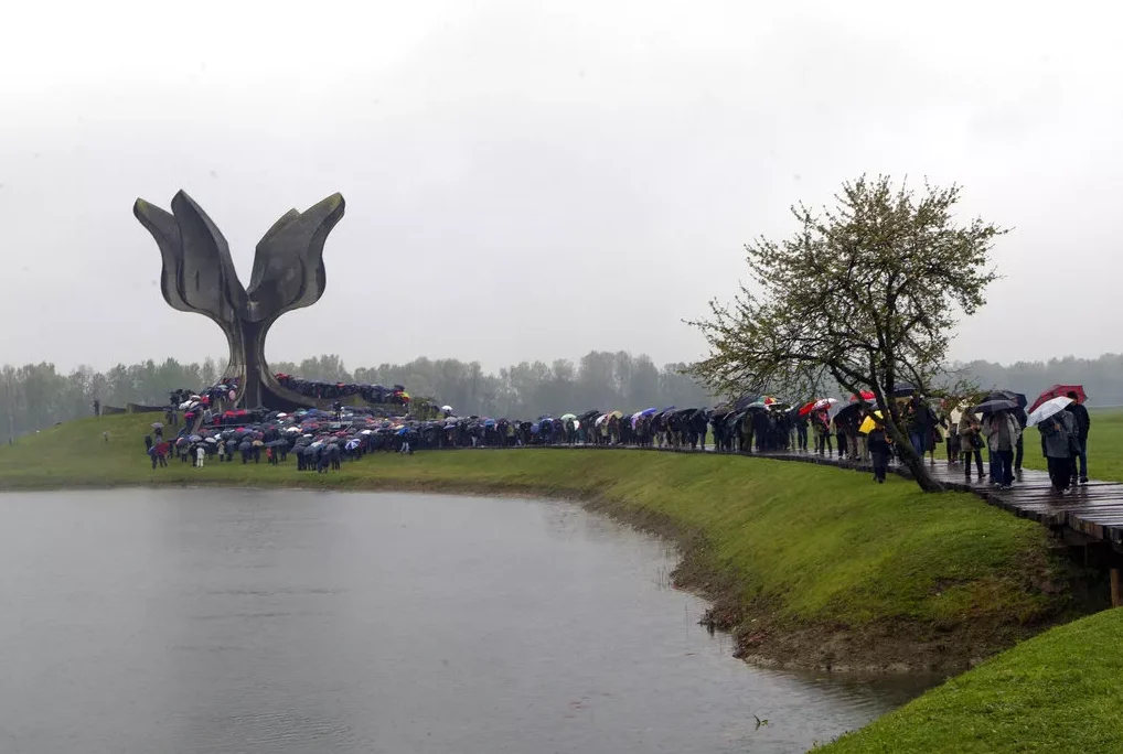 Grupacija ljudi sa kišobranima pred spomenikom