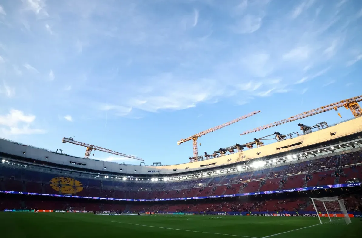 Veliki fudbalski stadion sa dizalicama iznad tribina i plavim nebom sa oblacima