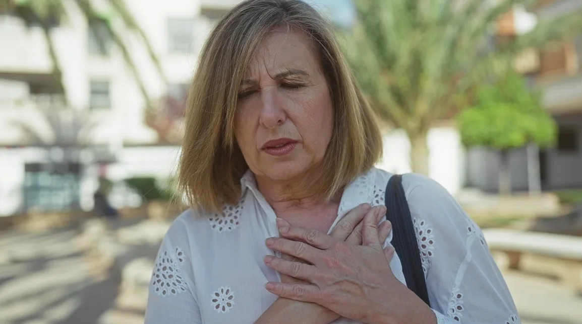 Starija žena sa rukama na grudima, zatvorenih očiju, pokazuje bol ili nelagodu.