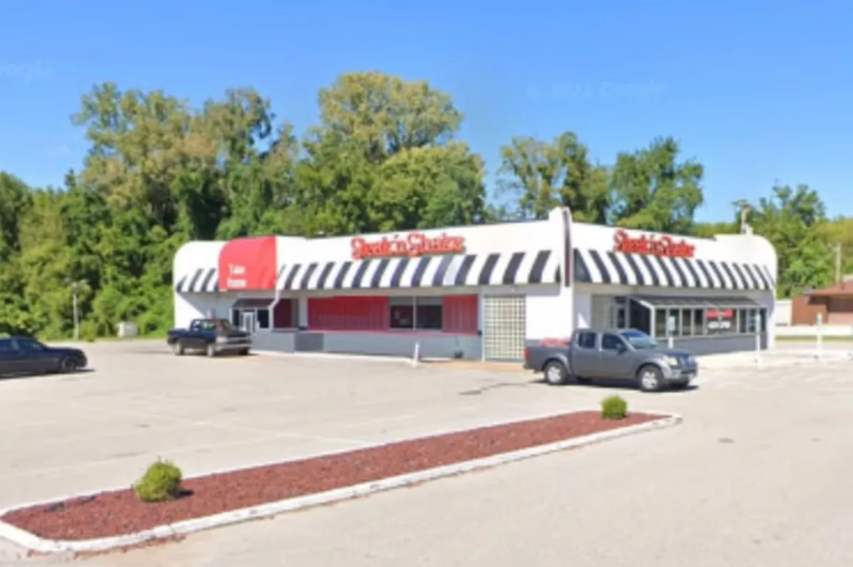 Vanjski izgled restorana Steak 'n Shake sa crnim i bijelim prugastim tendama i crvenim akcentima.