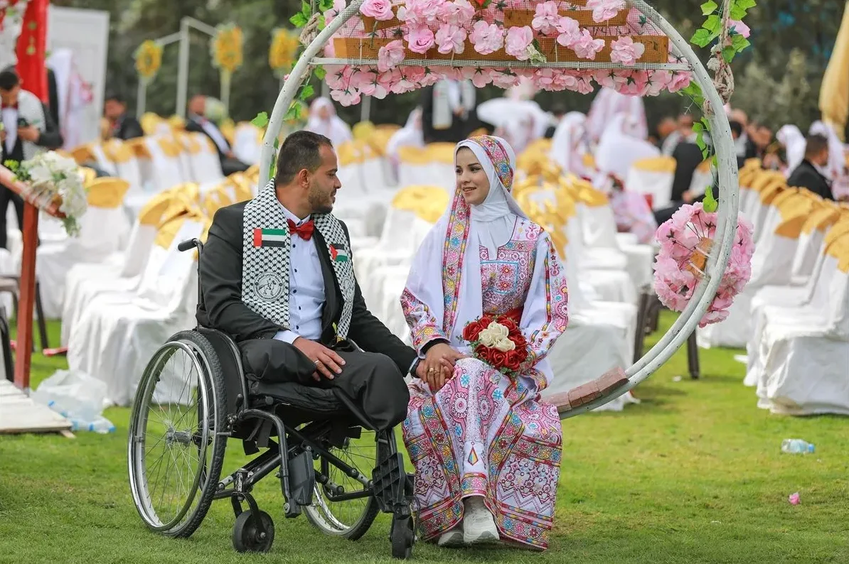 Mladenci, mladoženja u invalidskim kolicima, pozdravljaju goste na vjenčanju na otvorenom