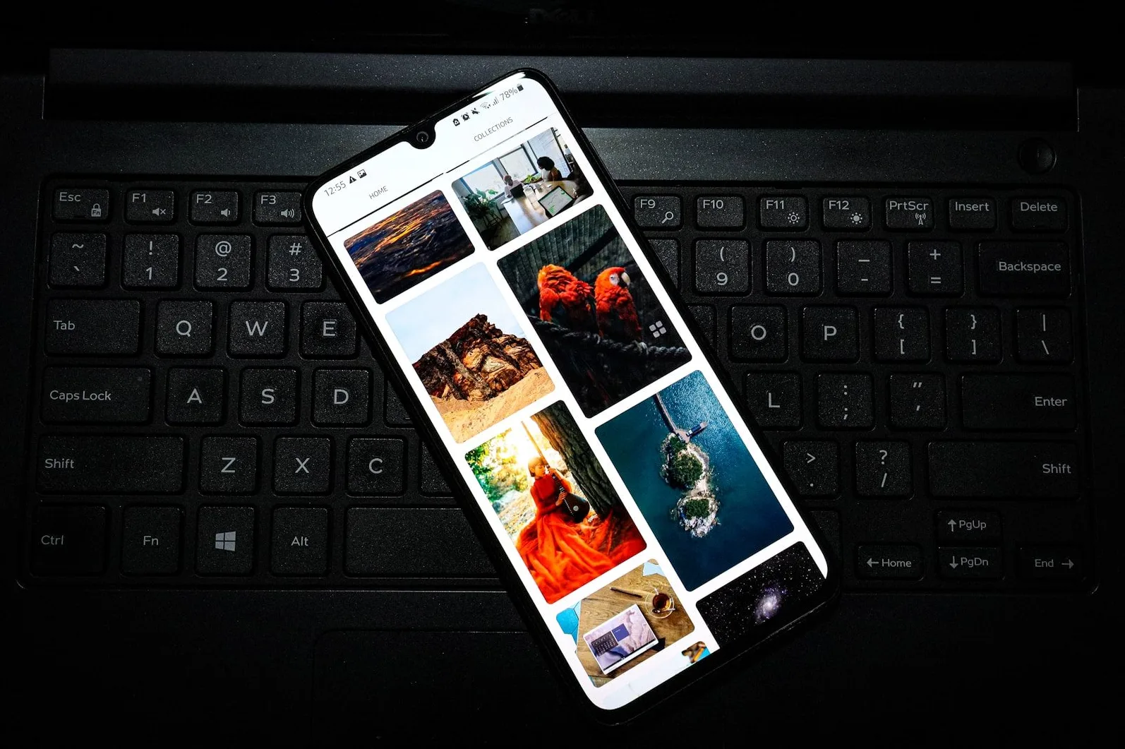 Pametni telefon sa kolekcijom slika na ekranu, postavljen na crnu tastaturu laptopa.