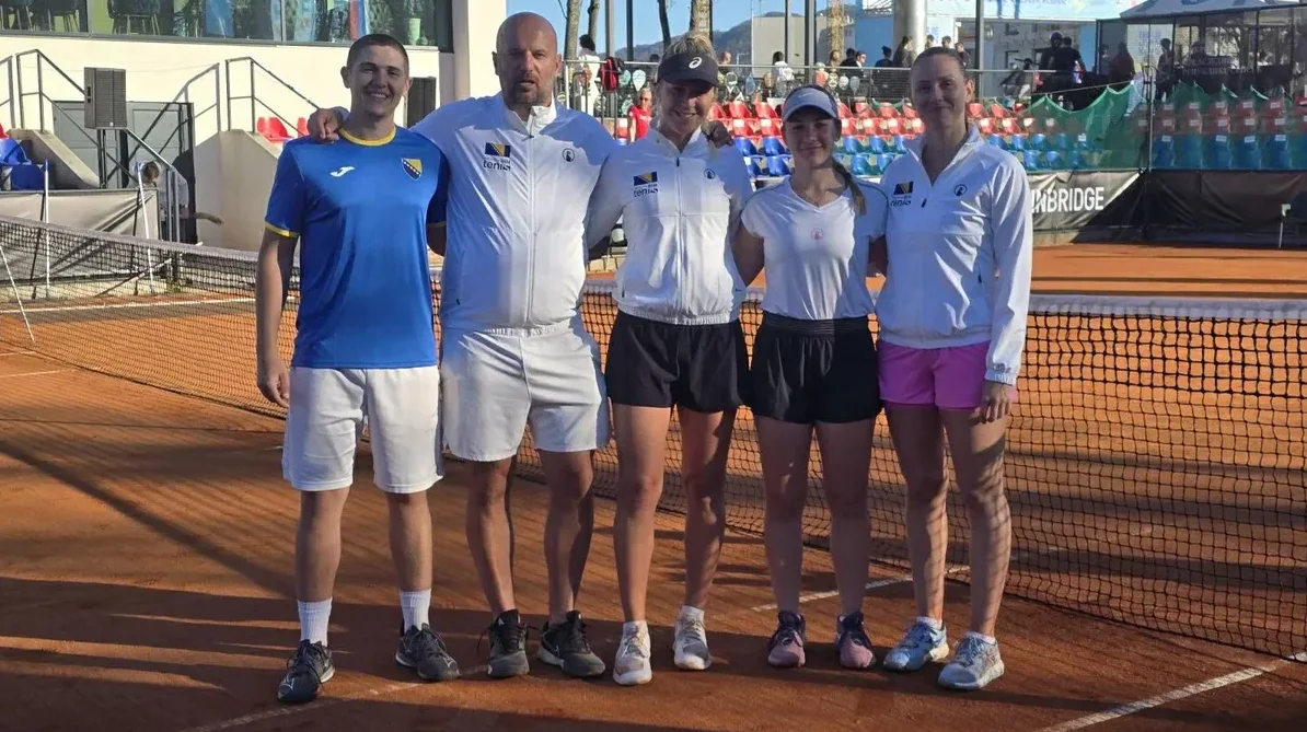 Petoro tenisera u bijelim i plavim majicama stoje ispred mreže na teniskom terenu.