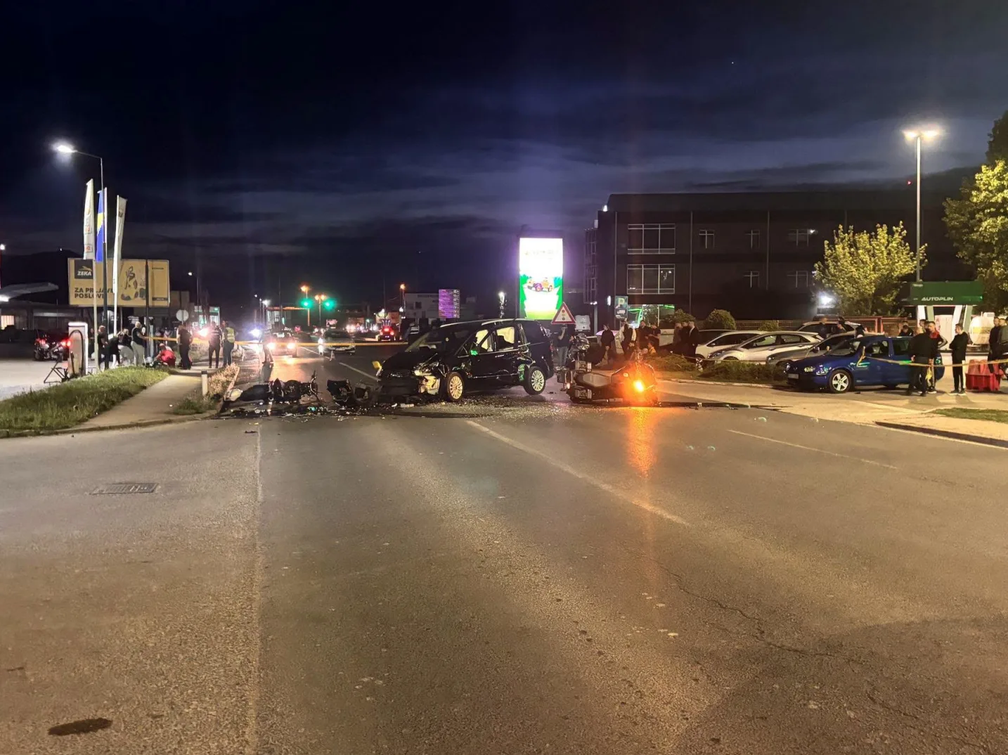 Teška saobraćajna nesreća sa više vozila noću, prizor olupina vozila na raskrsnici uz prisustvo policije i ljudi.