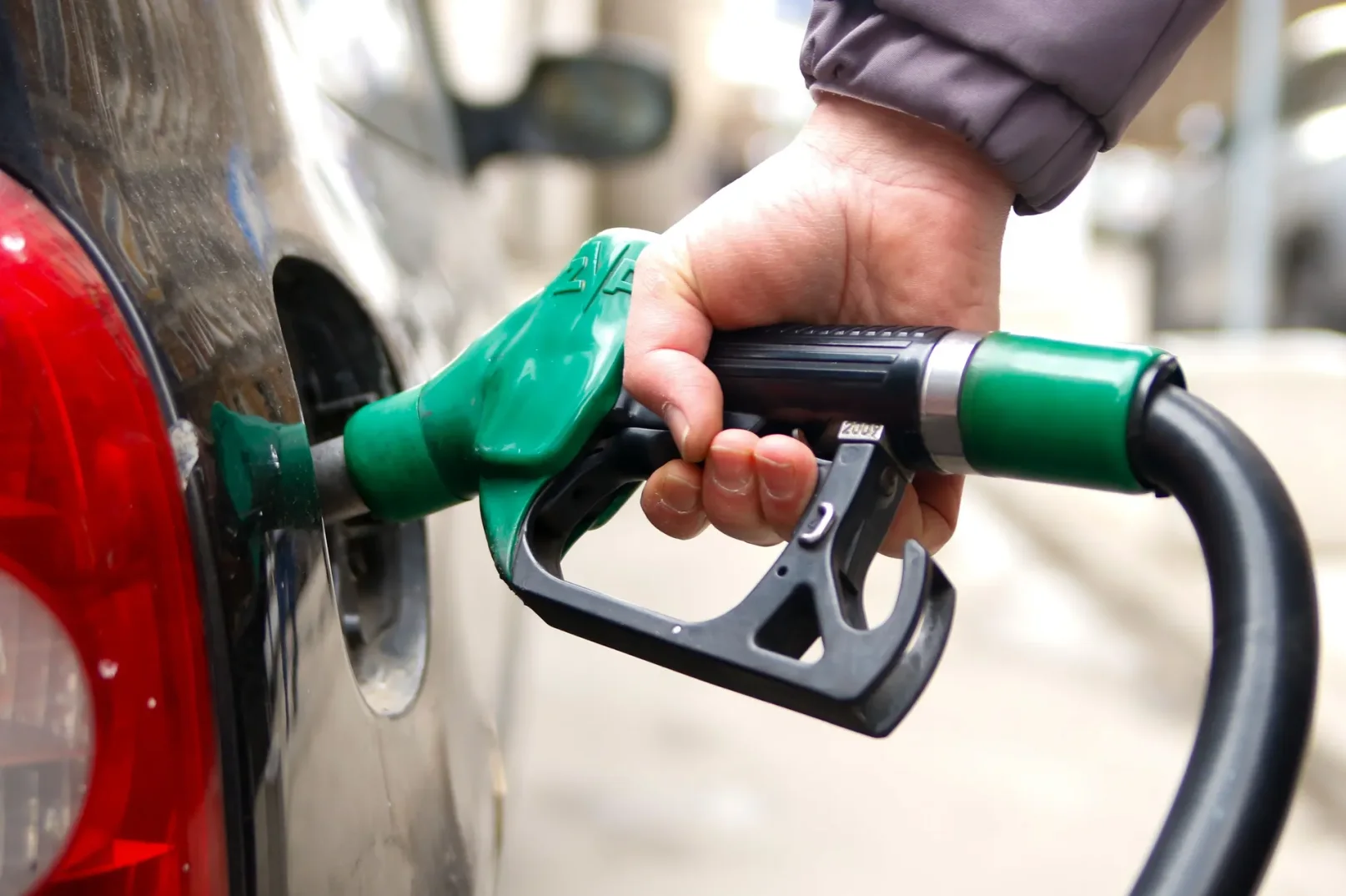 Ruka drži pištolj za točenje goriva dok puni rezervoar automobila.