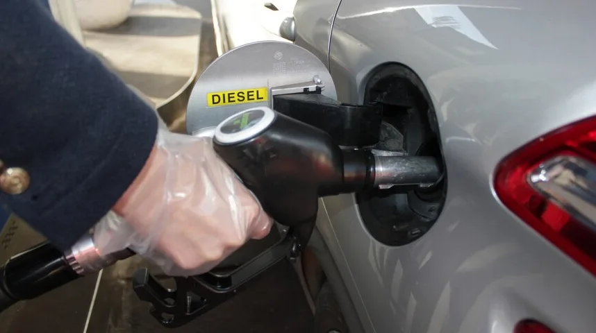 Ruka u rukavici drži dizel pištolj tokom točenja goriva u srebrni automobil.