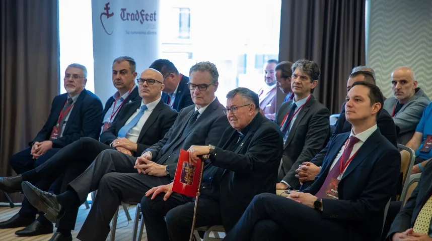 Grupa muškaraca u odijelima i sjemenišnoj odjeći sjedi u publici tokom konferencije.